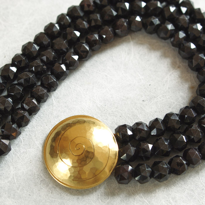 Das Collier aus der Kollektion "Schnecken" besteht aus Granat-Edelsteinen und einer geschmiedeten, vergoldeten Schnecke als Verschluss.