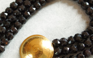 Das Collier aus der Kollektion "Schnecken" besteht aus Granat-Edelsteinen und einer geschmiedeten, vergoldeten Schnecke als Verschluss.